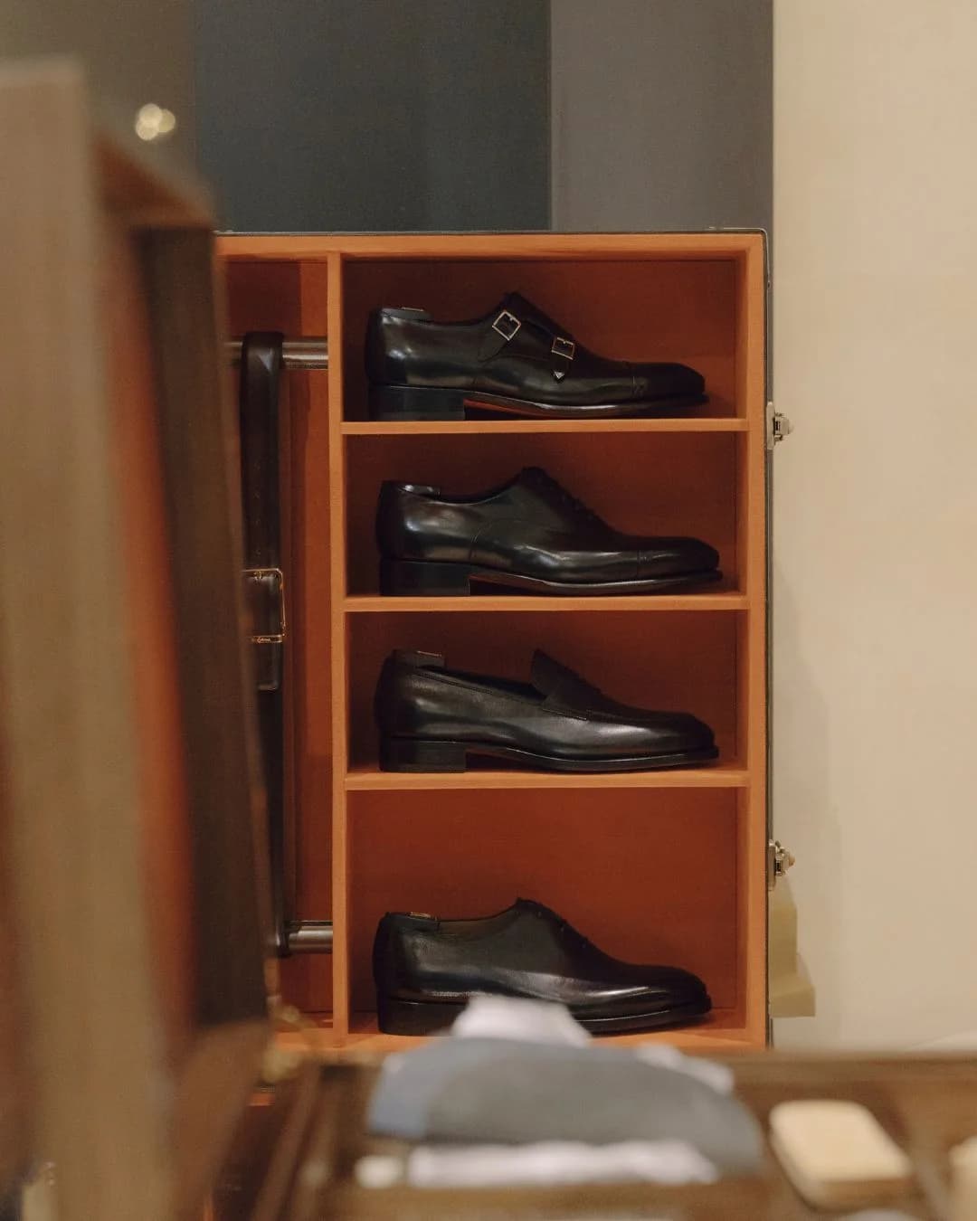Black Santoni leather shoes displayed inside a wooden care cabinet
