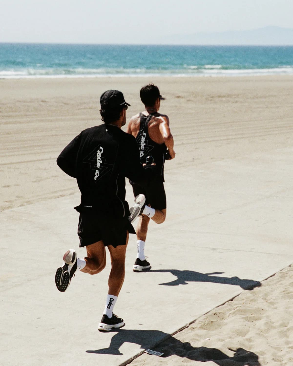 Two runners wearing Cadence x 247 apparel on a beach