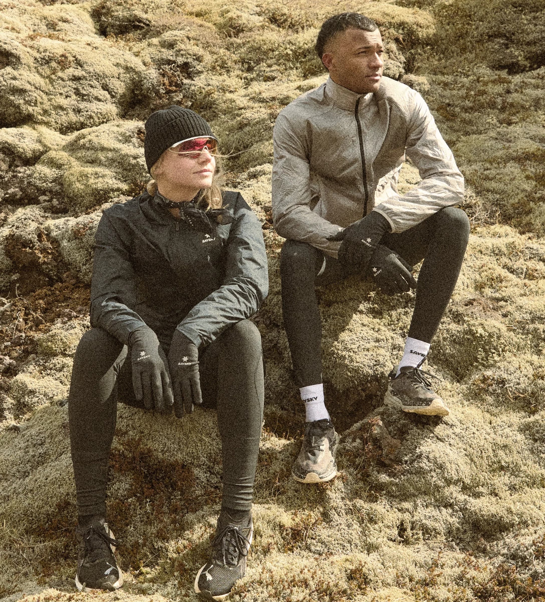 Two runners in SAYSKY outerwear and gloves sitting on rocky terrain
