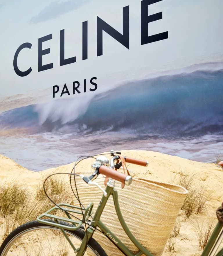 Green CELINE bicycle with a woven basket in front of an ocean-wave mural