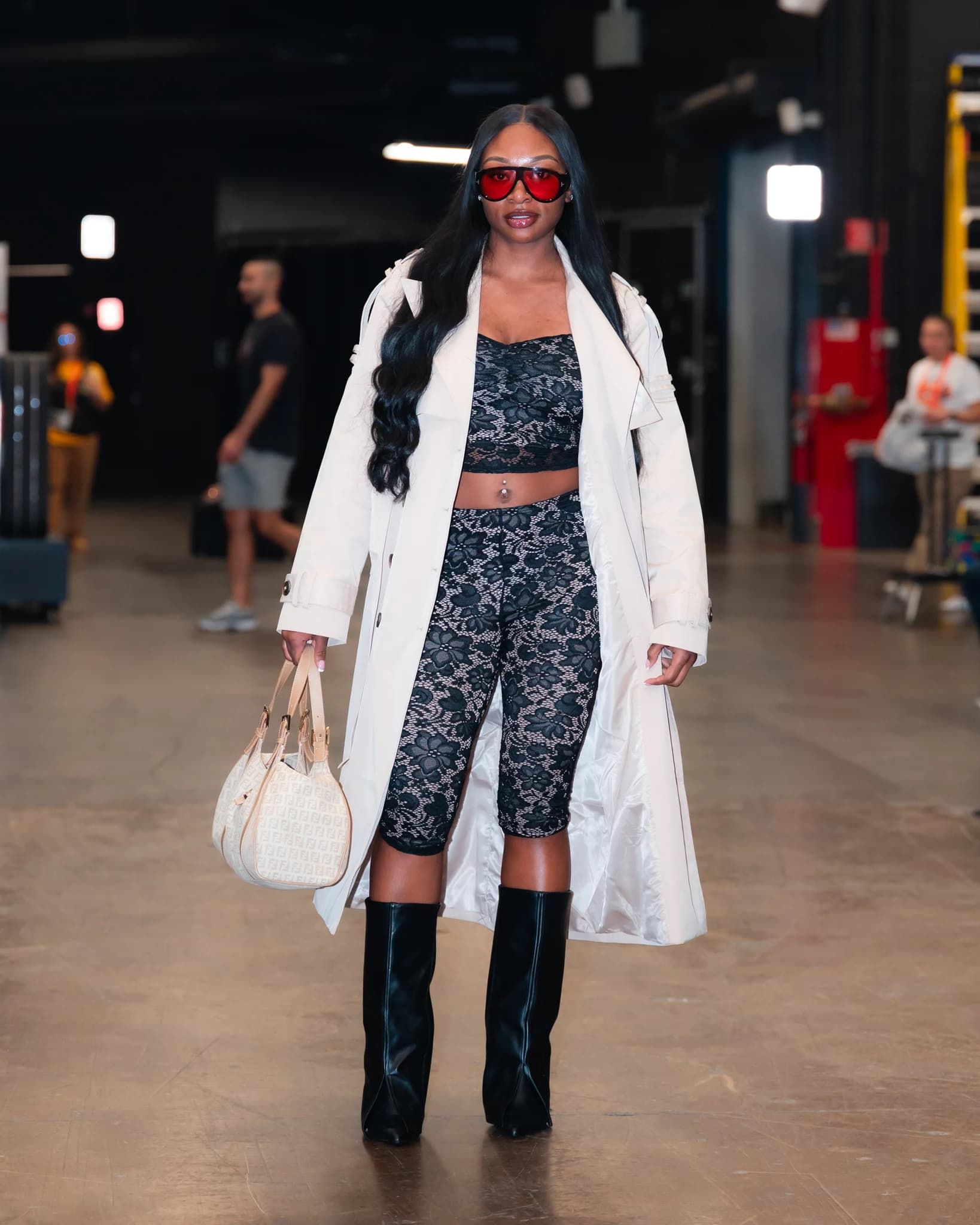 Dana Evans wears a white coat over a black lace outfit with knee-high boots and red sunglasses.