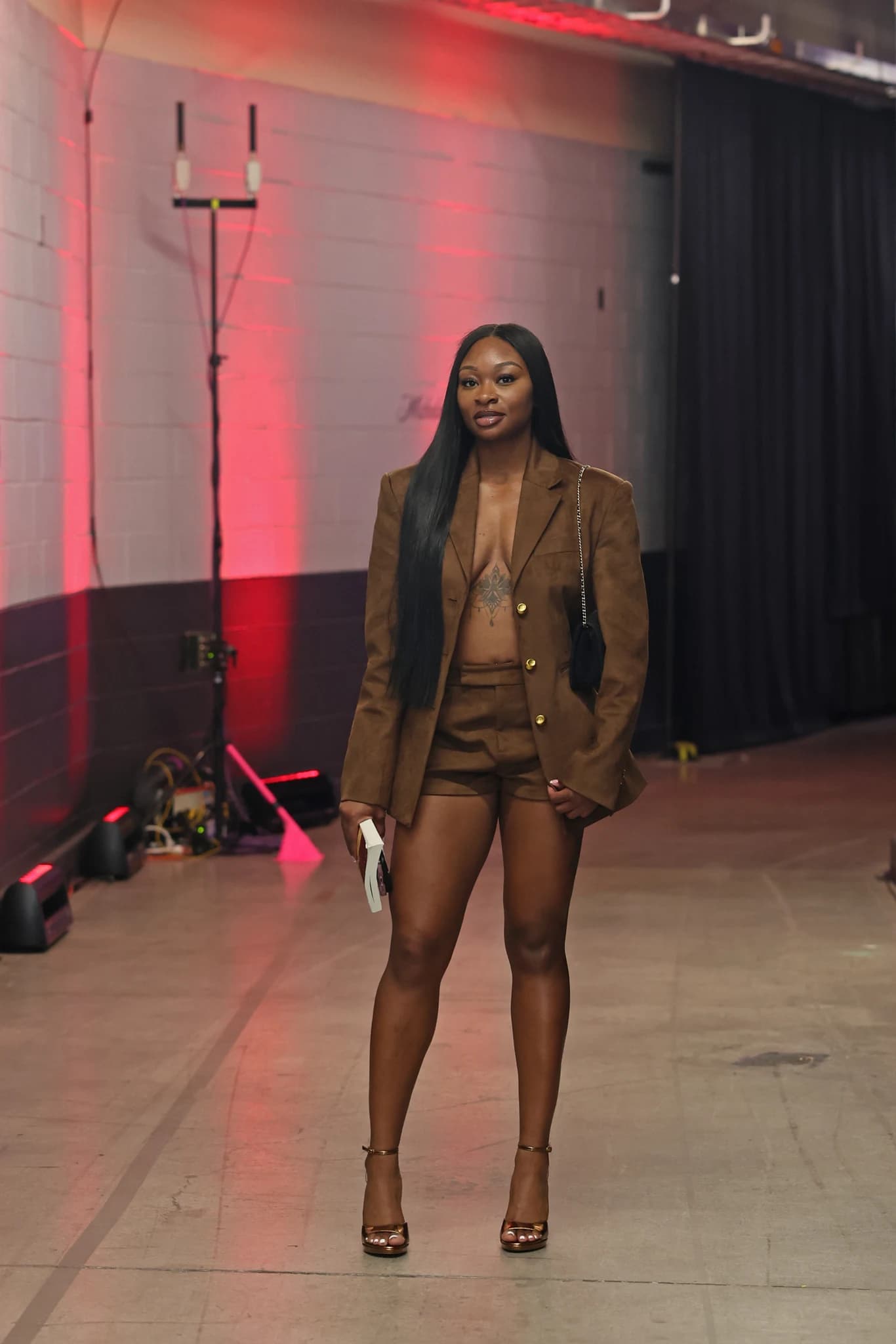 Dana Evans wears a brown blazer and shorts with metallic heels and a black shoulder bag.