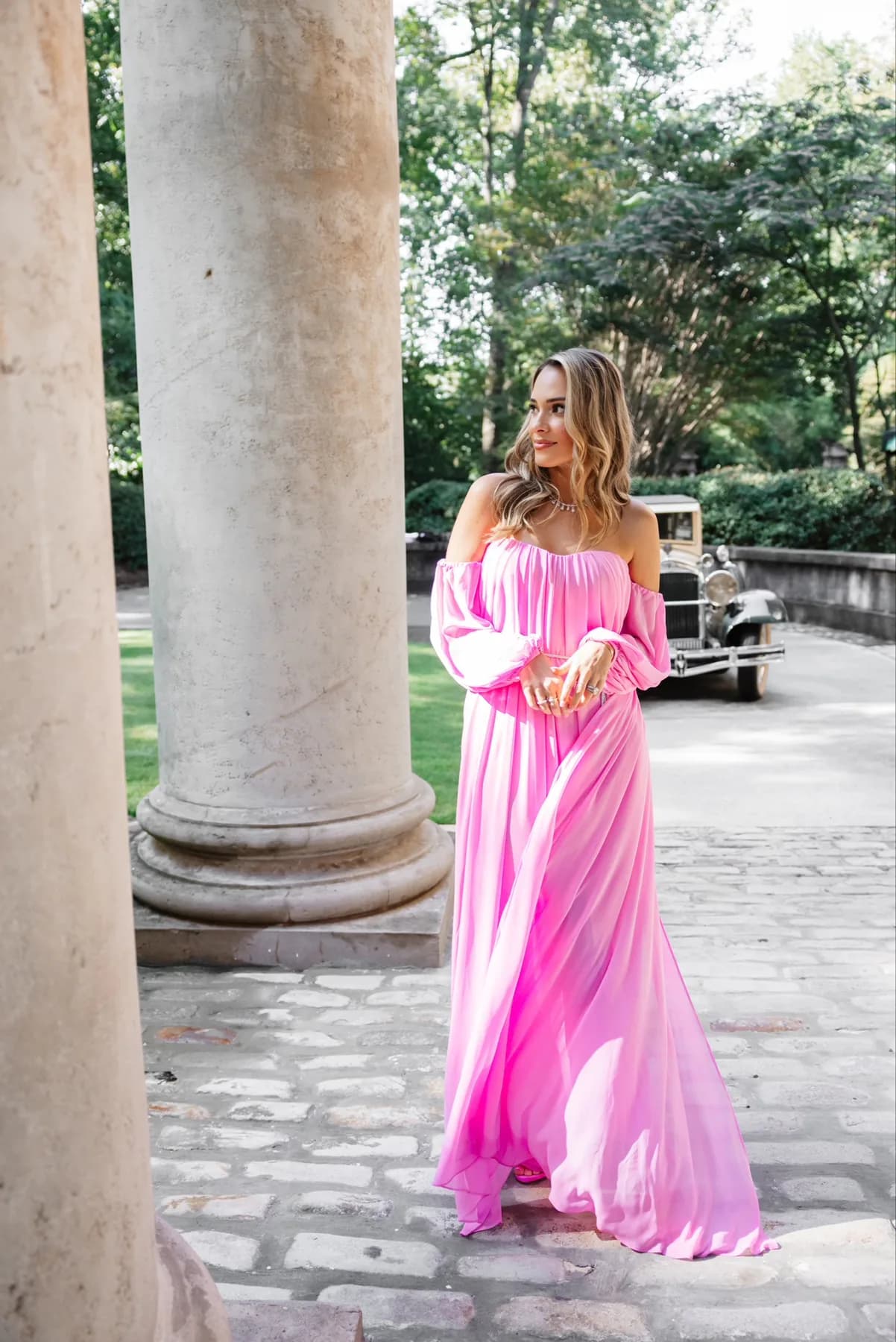 Model in a bright pink off-the-shoulder gown posing between stone columns