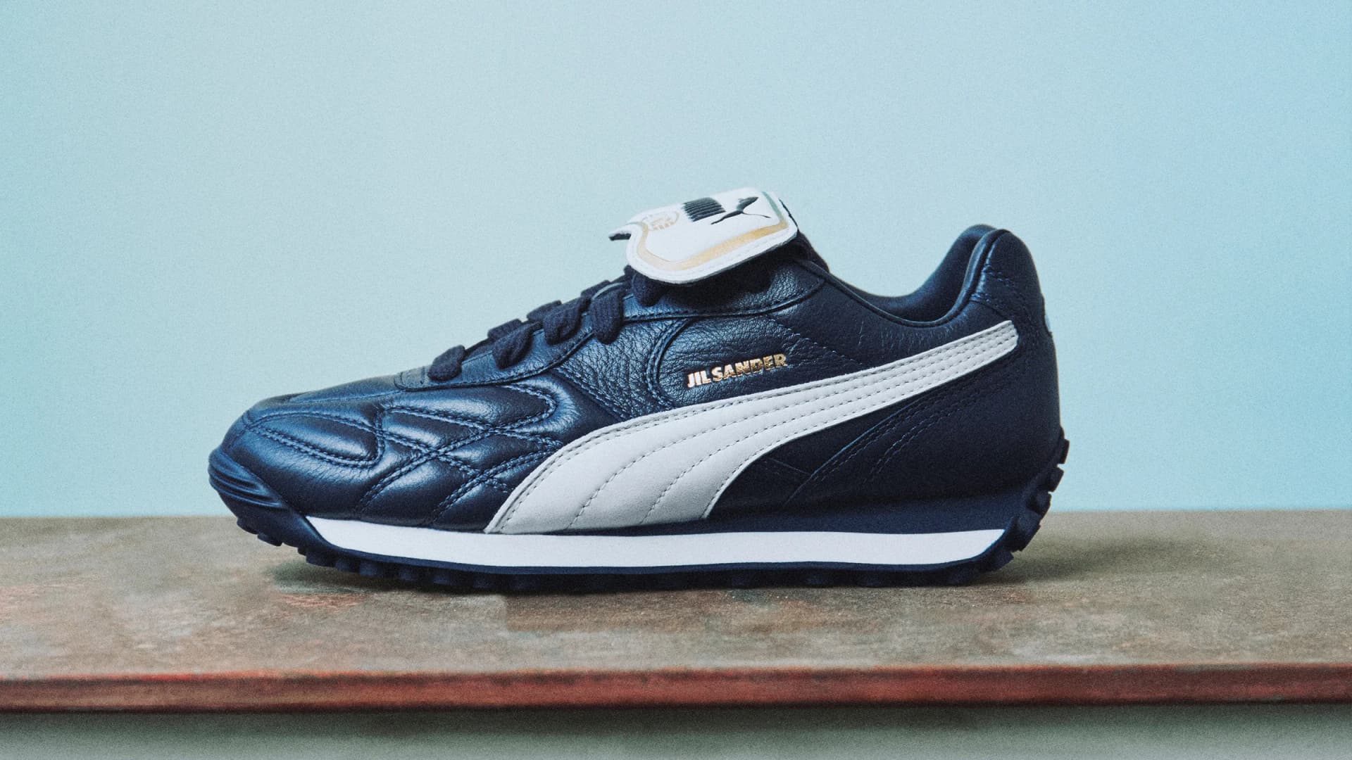 Navy leather Jil Sander x PUMA King Avanti sneaker with a white Formstrip and gold branding.