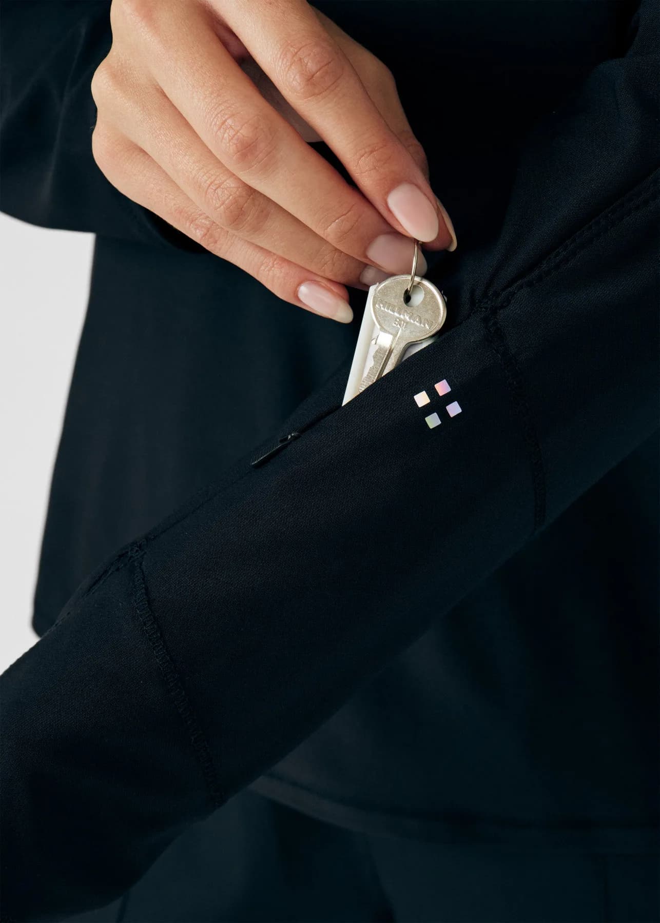 Close-up of keys being placed in a zippered black scrub pocket