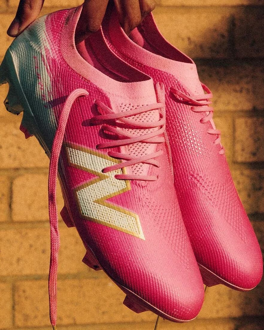 Pair of pink New Balance Furon v8 football boots held by their heels