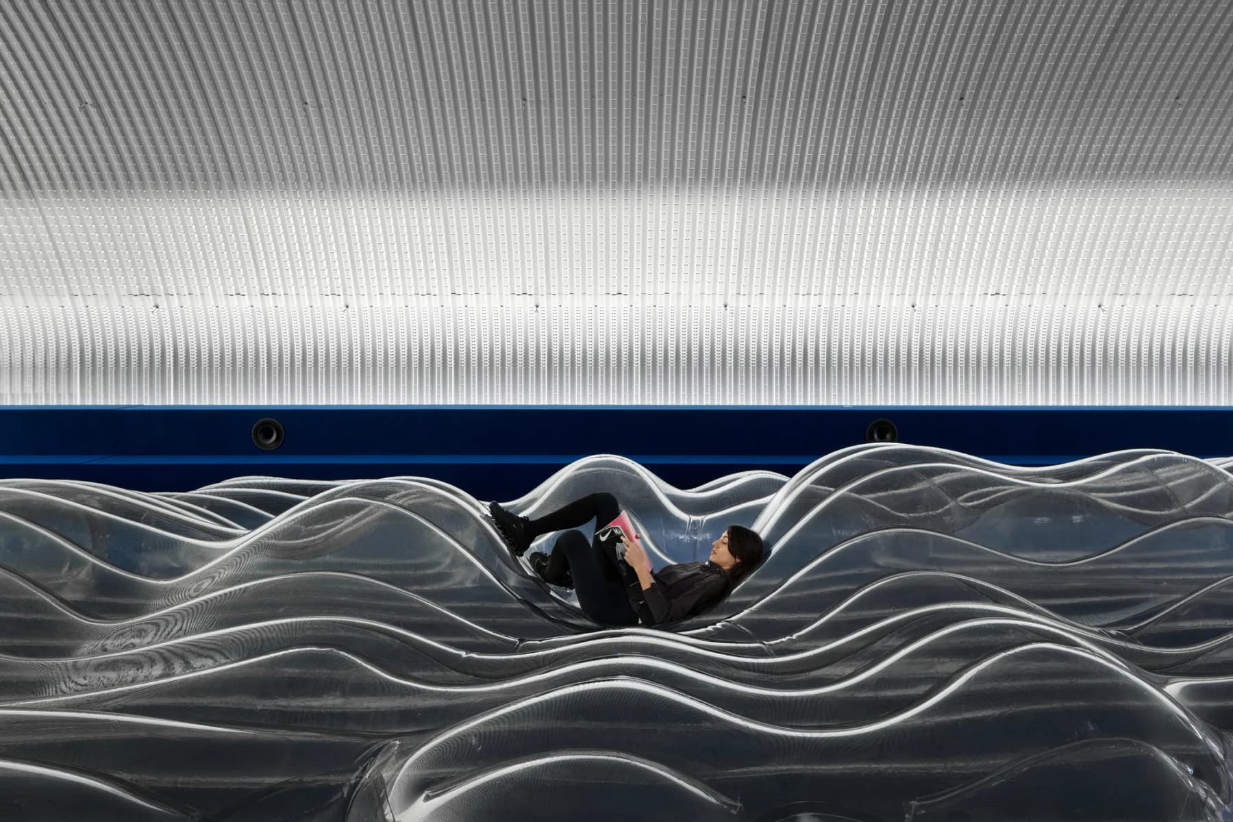 Visitor reclining inside a transparent wave-shaped Nike Air installation