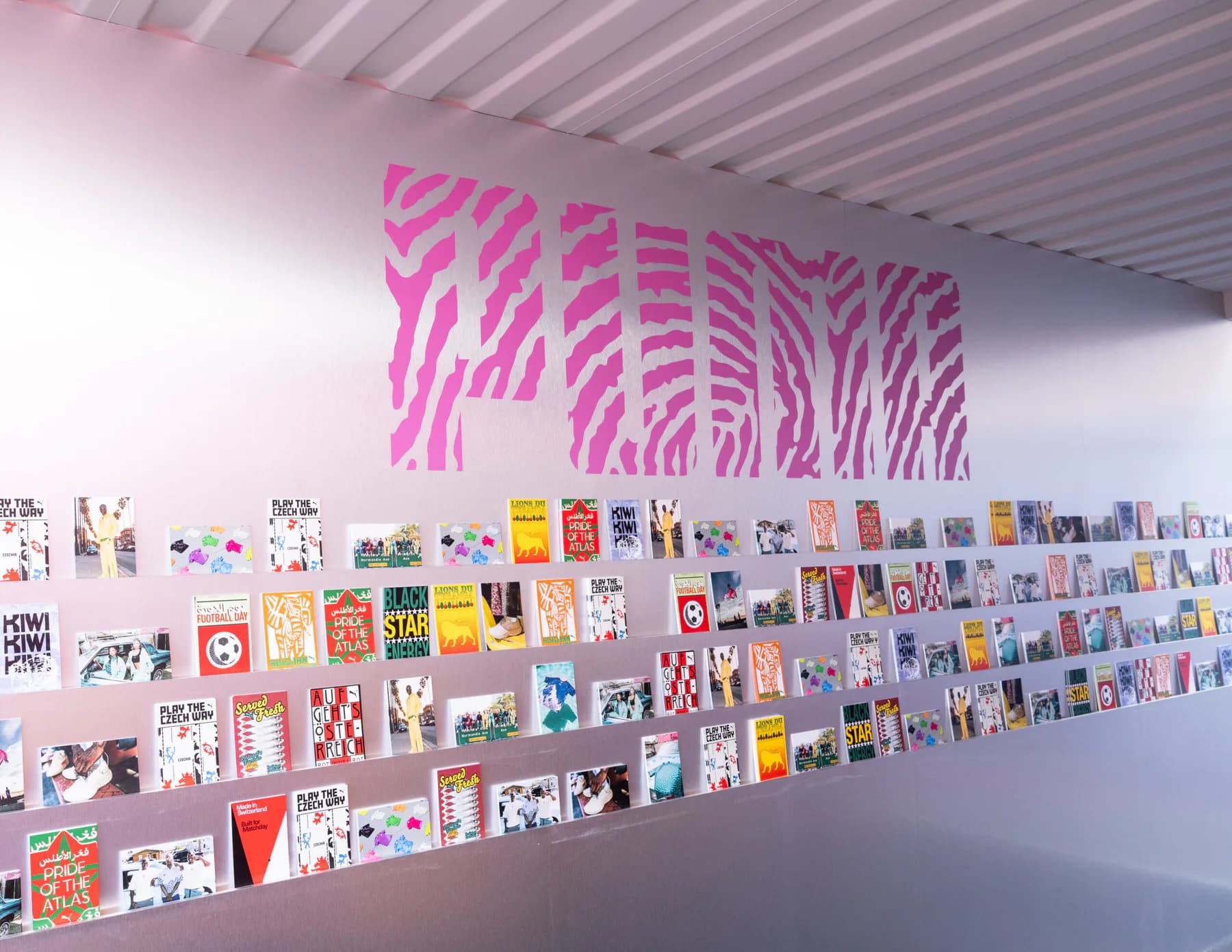 PUMA x Salehe Bembury zines displayed beneath a pink PUMA wall graphic