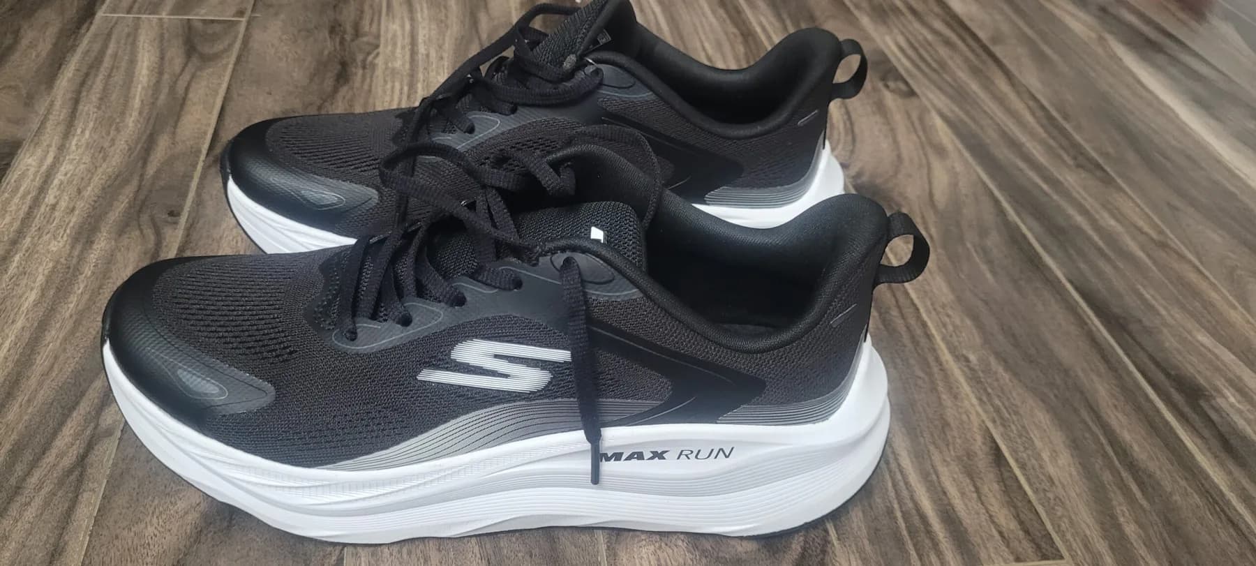 Black Skechers Max Run Pacewave shoes with white midsoles on a wood floor