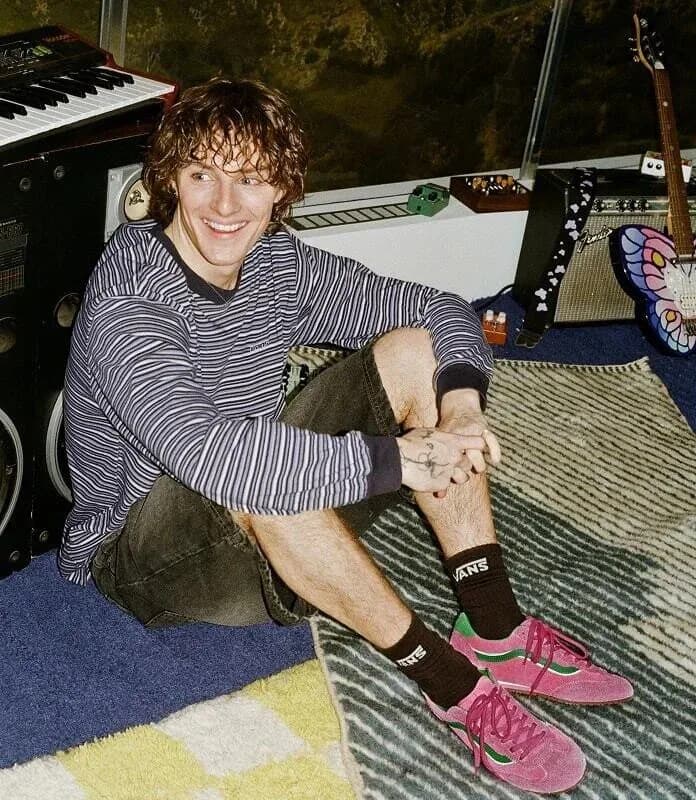 Young man in pink Vans sneakers seated beside musical equipment