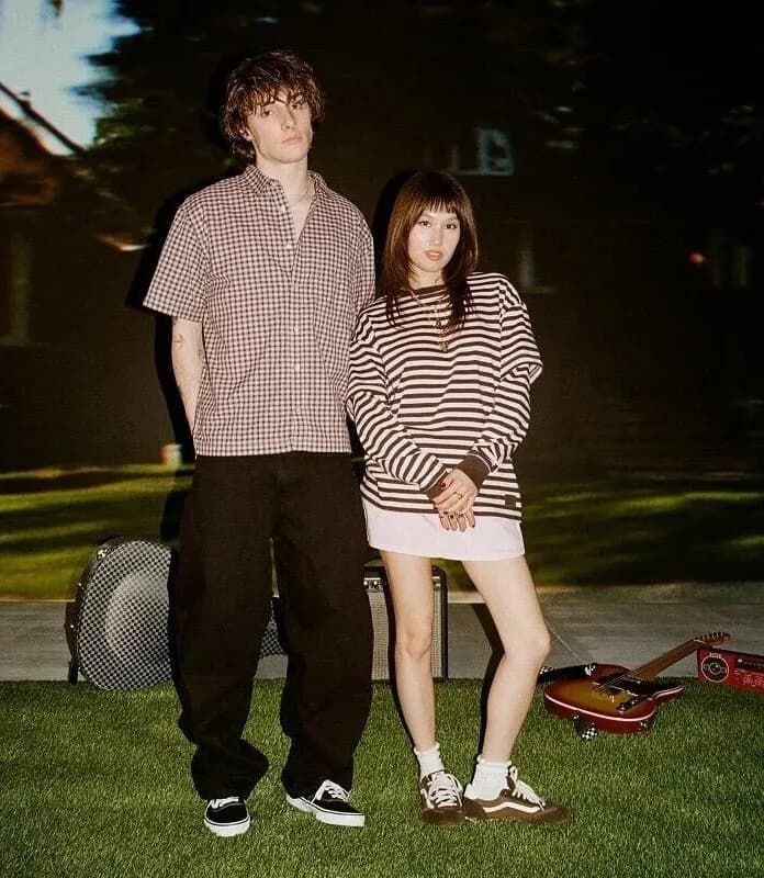 Two models wearing Vans sneakers pose outdoors beside a guitar